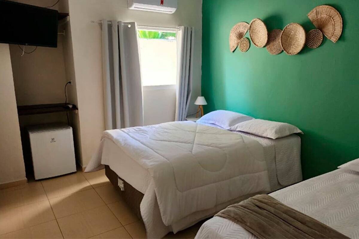 Habitación de hotel con dos camas, un escritorio pequeño, un televisor y una pared verde con cestas tejidas.