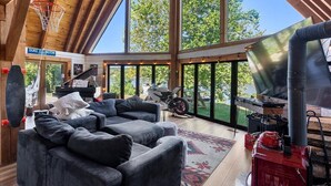 A spacious living room with a large gray sectional sofa, a basketball hoop, a piano, and a grill area.