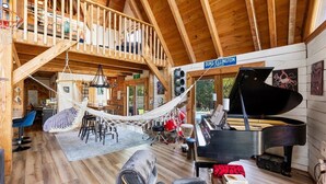 A spacious living area with a grand piano, a hammock, and a high wooden ceiling.