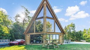 A wooden cabin with a triangular roof, large windows, and a picnic table in the foreground.