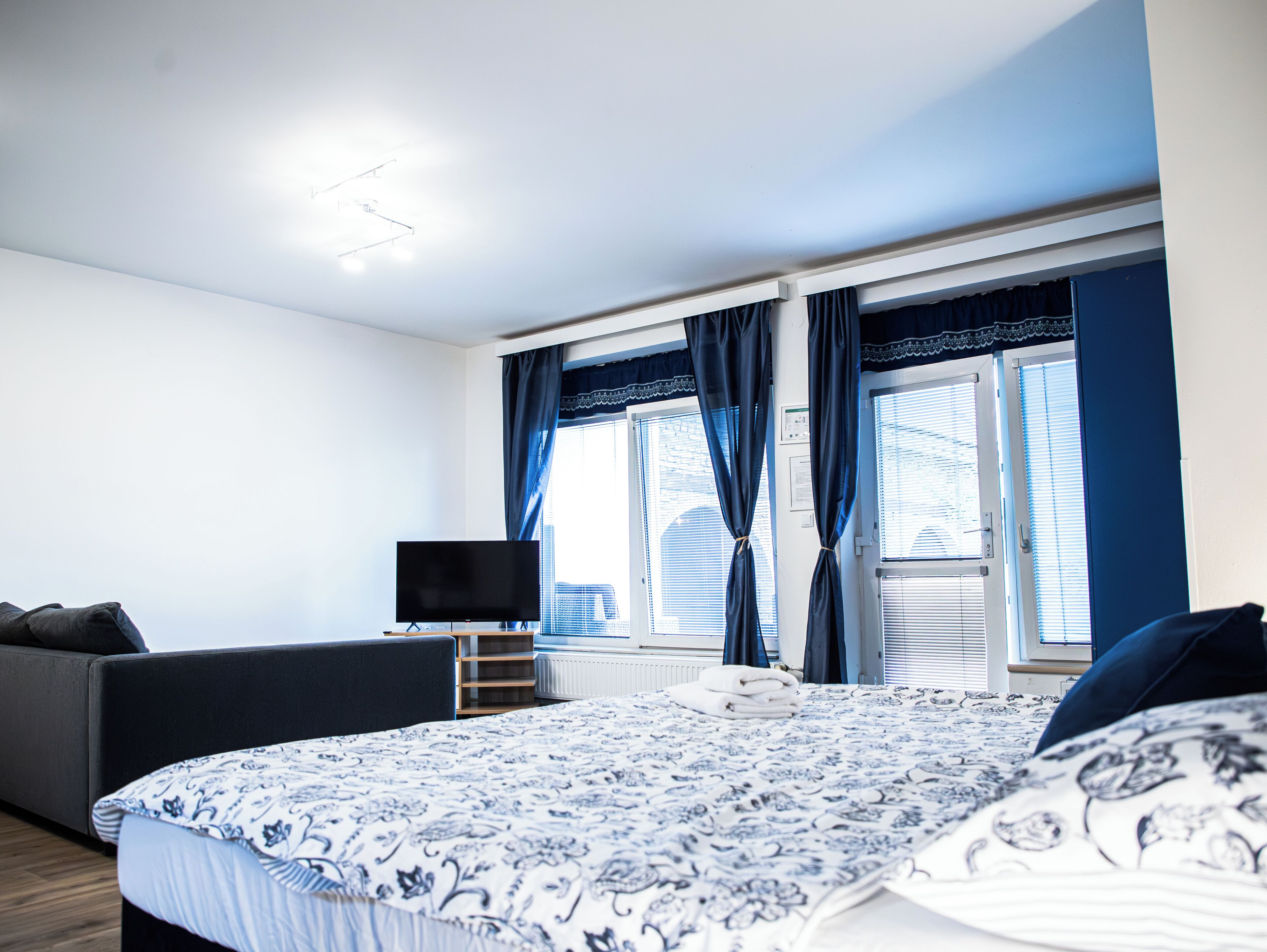 A modern bedroom with a large bed, a flat-screen TV, a sofa, and a window with curtains.