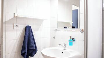 A bathroom with white tiles, a white sink, a blue towel, and a mirror.
