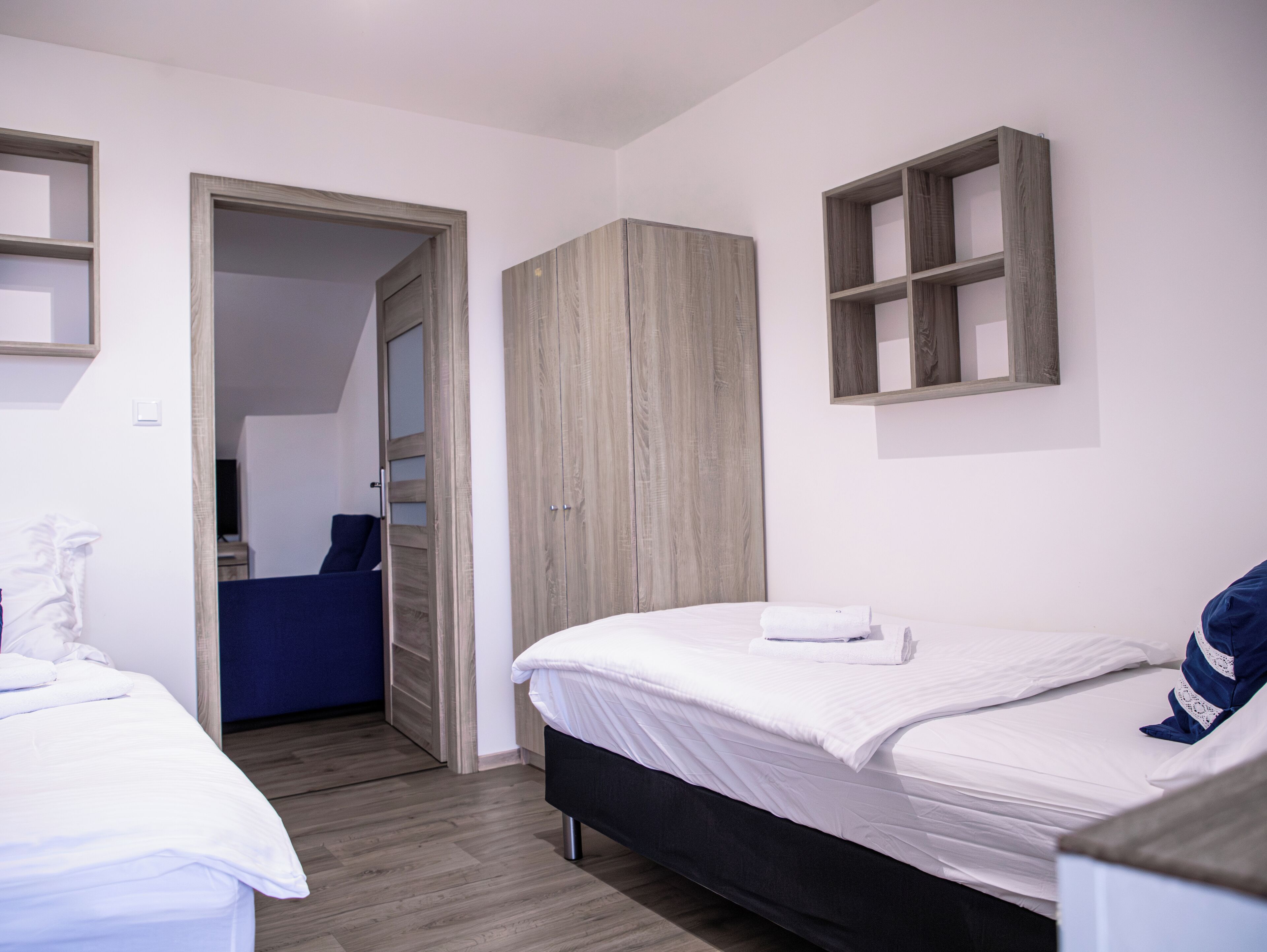 A bedroom with two beds, a wardrobe, and a small shelf.