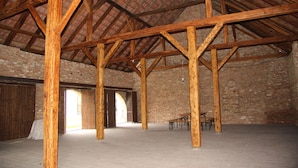 An interior with exposed wooden beams, brick walls, and a high ceiling. There are tables and chairs in the center. - Penzion Posada Podivín (Podivin)