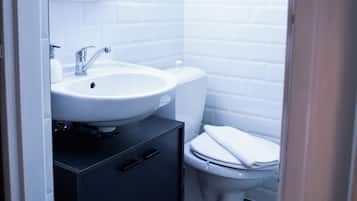 Une petite salle de bain avec un lavabo blanc, des toilettes et un meuble de couleur sombre.