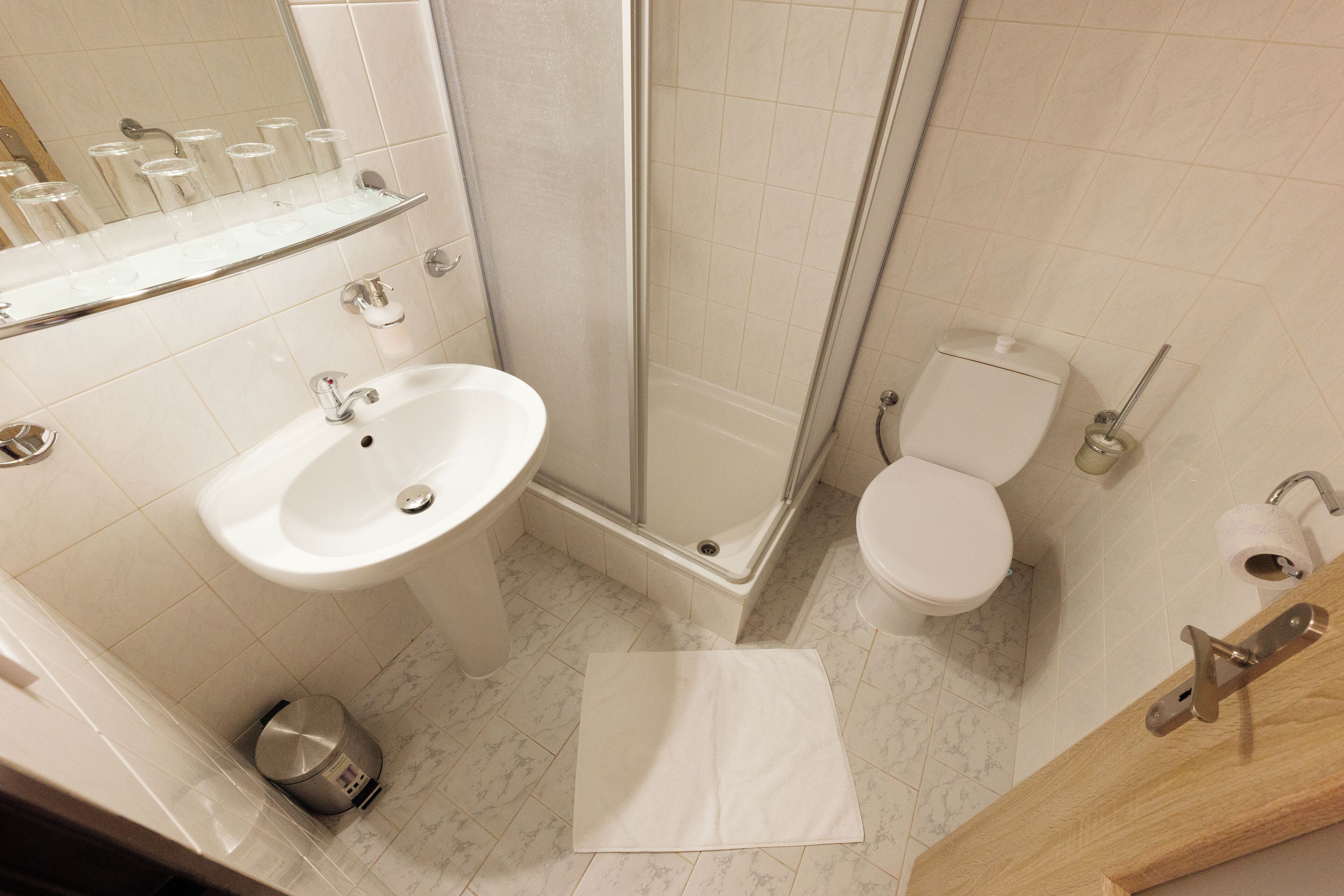 A bathroom with a sink, toilet, shower, and a trash bin.