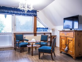 Una habitación con piso de madera, un candelabro, un televisor sobre un mueble de madera y una mesa con sillas.