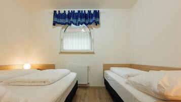 Habitación doble con dos camas, una ventana con cortina, un radiador y una mesita de noche.