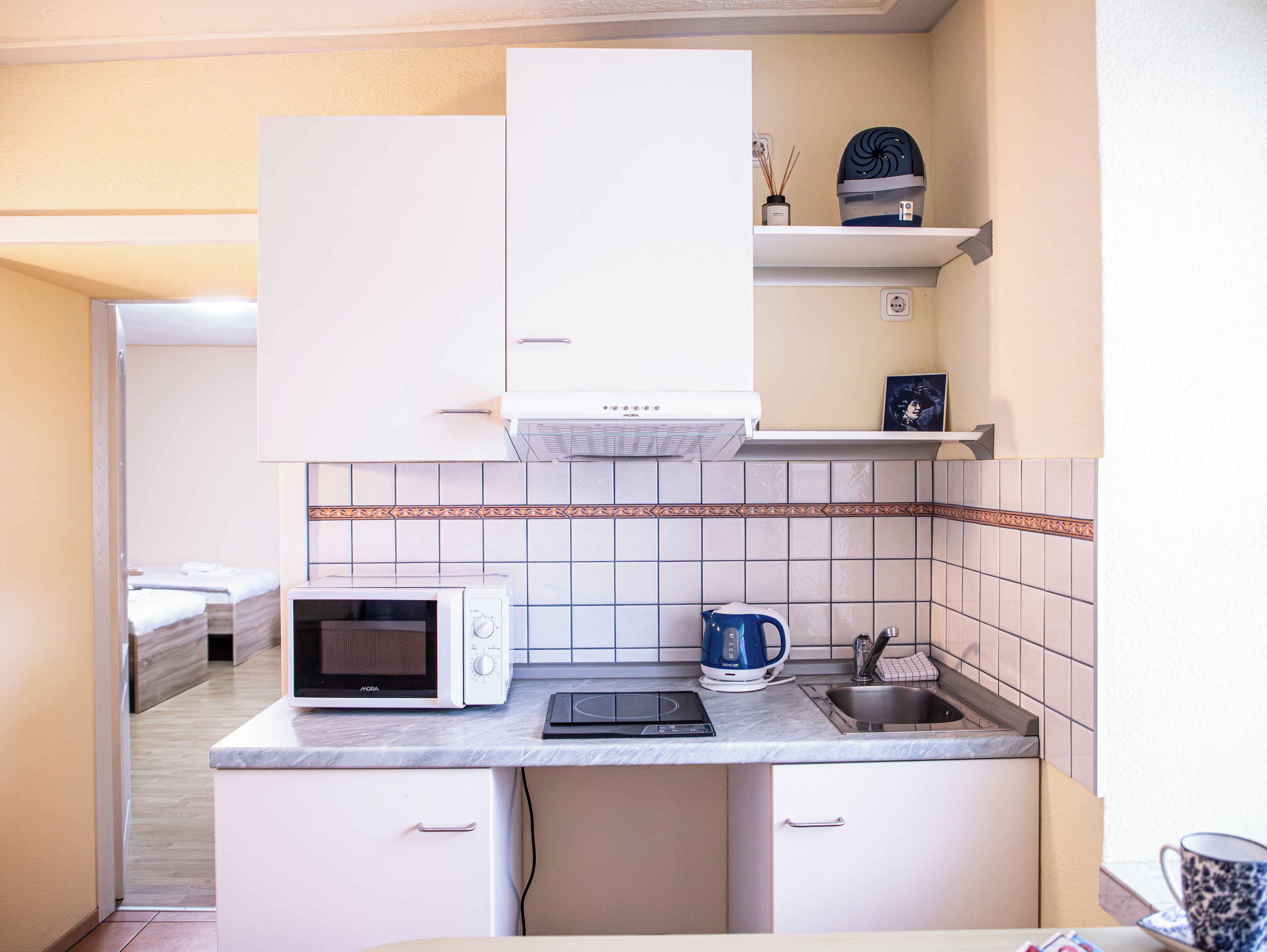 Una cocina compacta equipada con microondas, hervidor y un lavamanos pequeño.