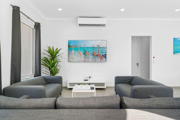 A modern living room with grey sofas, a white coffee table, and a painting of flamingos on the wall.