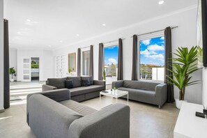 A modern living room with grey sofas, a white coffee table, and large windows with curtains.