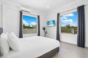 A bedroom with a bed, a window with curtains, a potted plant, and a painting on the wall. - 4 BR Paradise with Private Pool! (Noord)