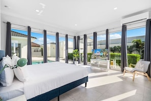 A modern bedroom with a large bed, a view of a swimming pool, and a balcony with a chair.