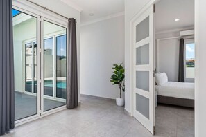 A modern room with a sliding glass door leading to a balcony, a potted plant, and a bed with a white headboard.