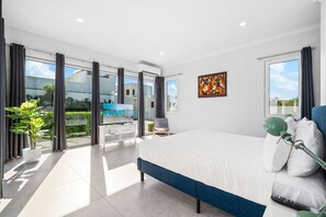 A modern bedroom with a large bed, a view of the sea, and a balcony with a chair. - Modern 4BR Pool Villa, Walk to Boca Catalina Bay (Noord)