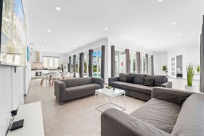 A modern living room with a sofa, coffee table, and a dining area with chairs and a table. - 4 BR Paradise with Private Pool! (Noord)