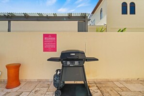 A portable grill with a gas tank and a red warning sign on a wall.