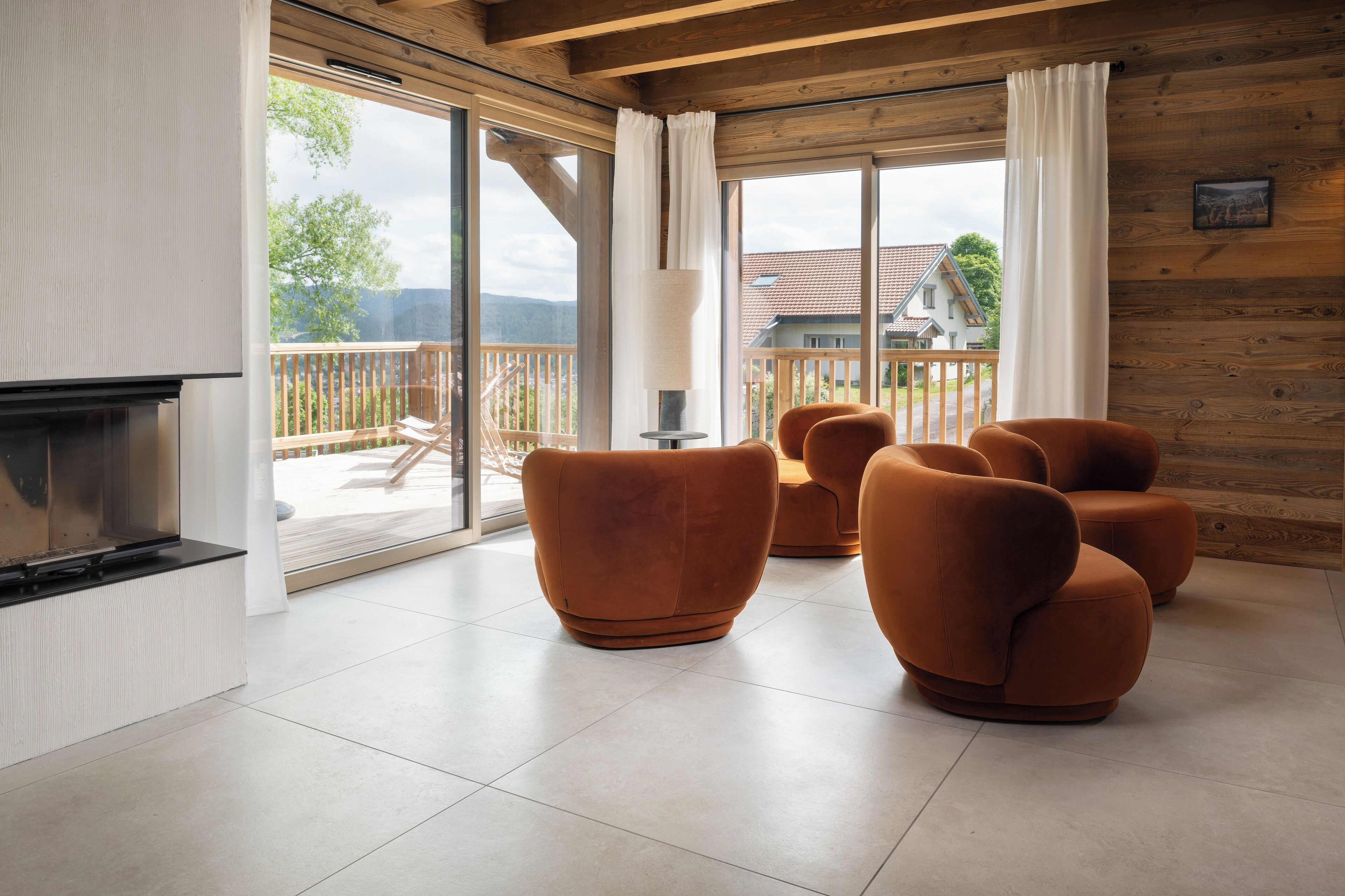 A modern living room with a fireplace, large windows, and a balcony with outdoor furniture.
