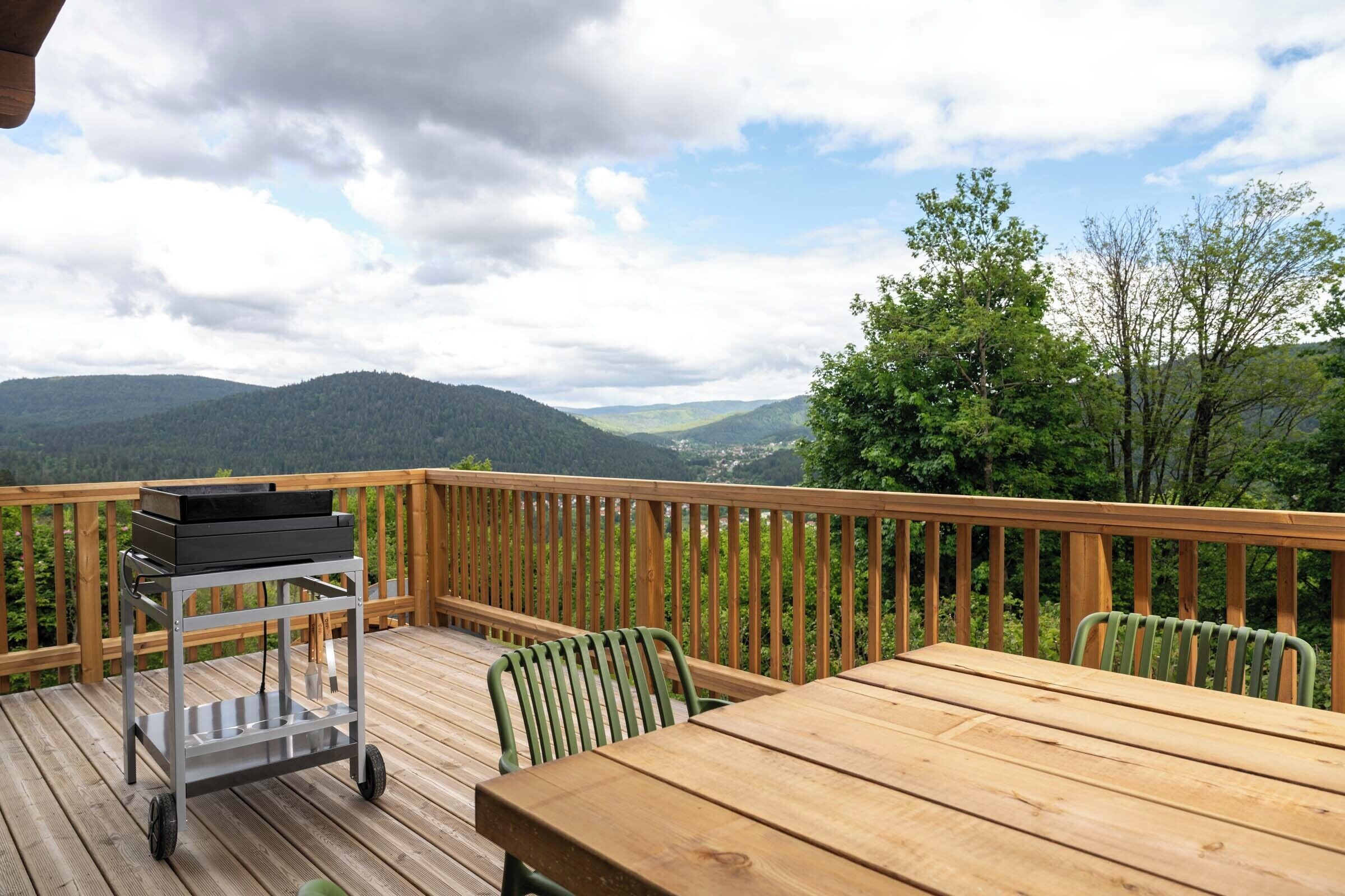 A wooden deck with a table and chairs, overlooking a mountainous landscape.