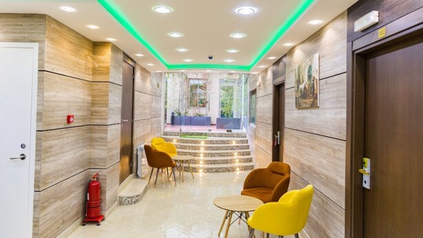 A hotel lobby with a marble floor, a staircase leading to a balcony, and yellow chairs. - HNR Hotel - El Hamma (Algiers)