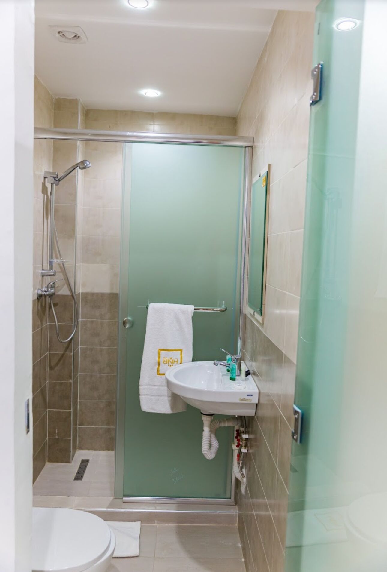 Un baño con cabina de ducha de vidrio, un lavamanos blanco con espejo y un inodoro.