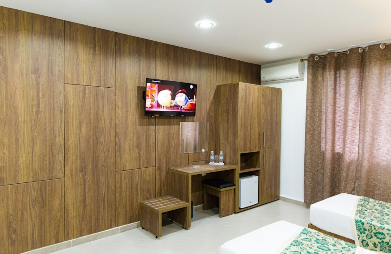 A modern room with wooden panel walls, a flat-screen TV, a small desk with a chair, a mini fridge, and a bed with patterned bedding.