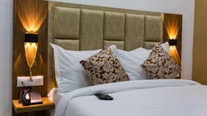 A hotel room with a tufted headboard, two patterned pillows, a bedside table with a telephone, and wall-mounted lamps. - HNR Hotel - El Hamma (Algiers)