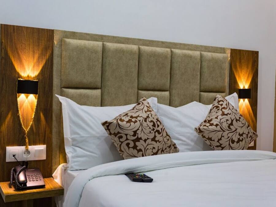 Habitación de hotel con cabecera capitonada, dos almohadas estampadas, una mesita de noche con teléfono y lámparas de pared.