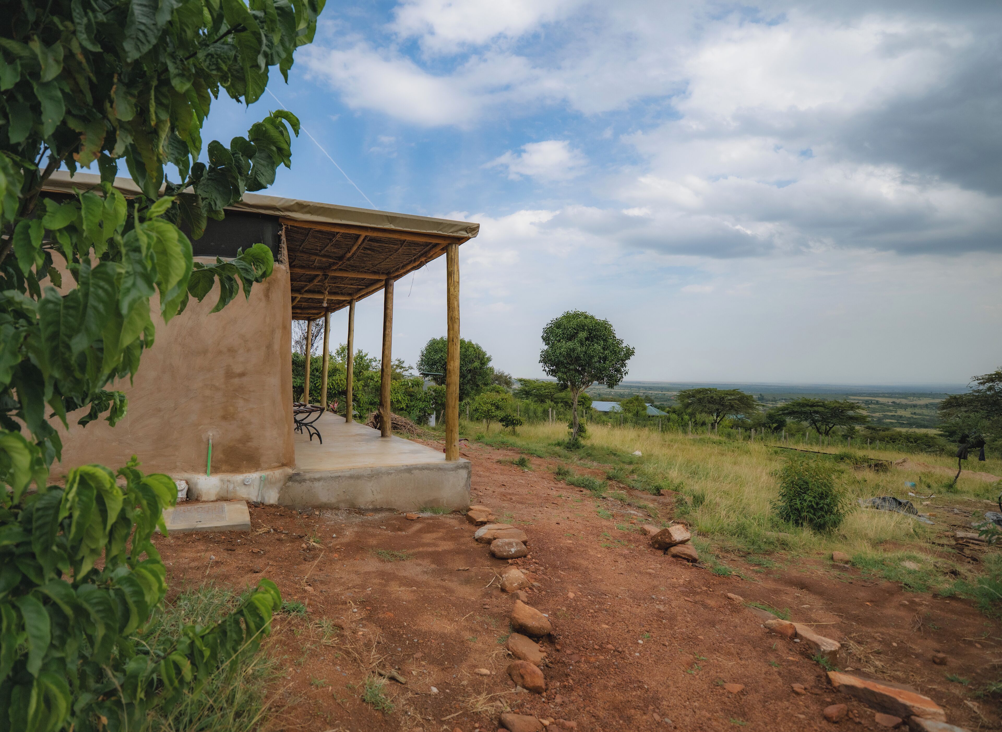 A rustic outdoor seating area with a wooden pergola, a concrete path, and a view of the landscape.