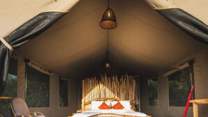 A tent with a wooden bed, a hanging light fixture, and a chair. - Mara hilltop (Maasai Mara)