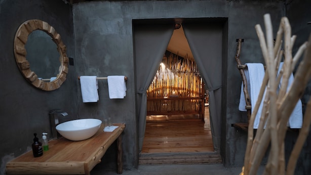 A rustic bathroom with a wooden vanity, a large round mirror, and a towel rack. - Mara hilltop (Maasai Mara)