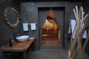 A rustic bathroom with a wooden vanity, a large round mirror, and a towel rack. - Mara hilltop (Maasai Mara)