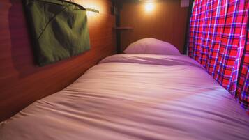 A single bed with a green bag hanging on the wall, a wooden headboard, and a plaid curtain.