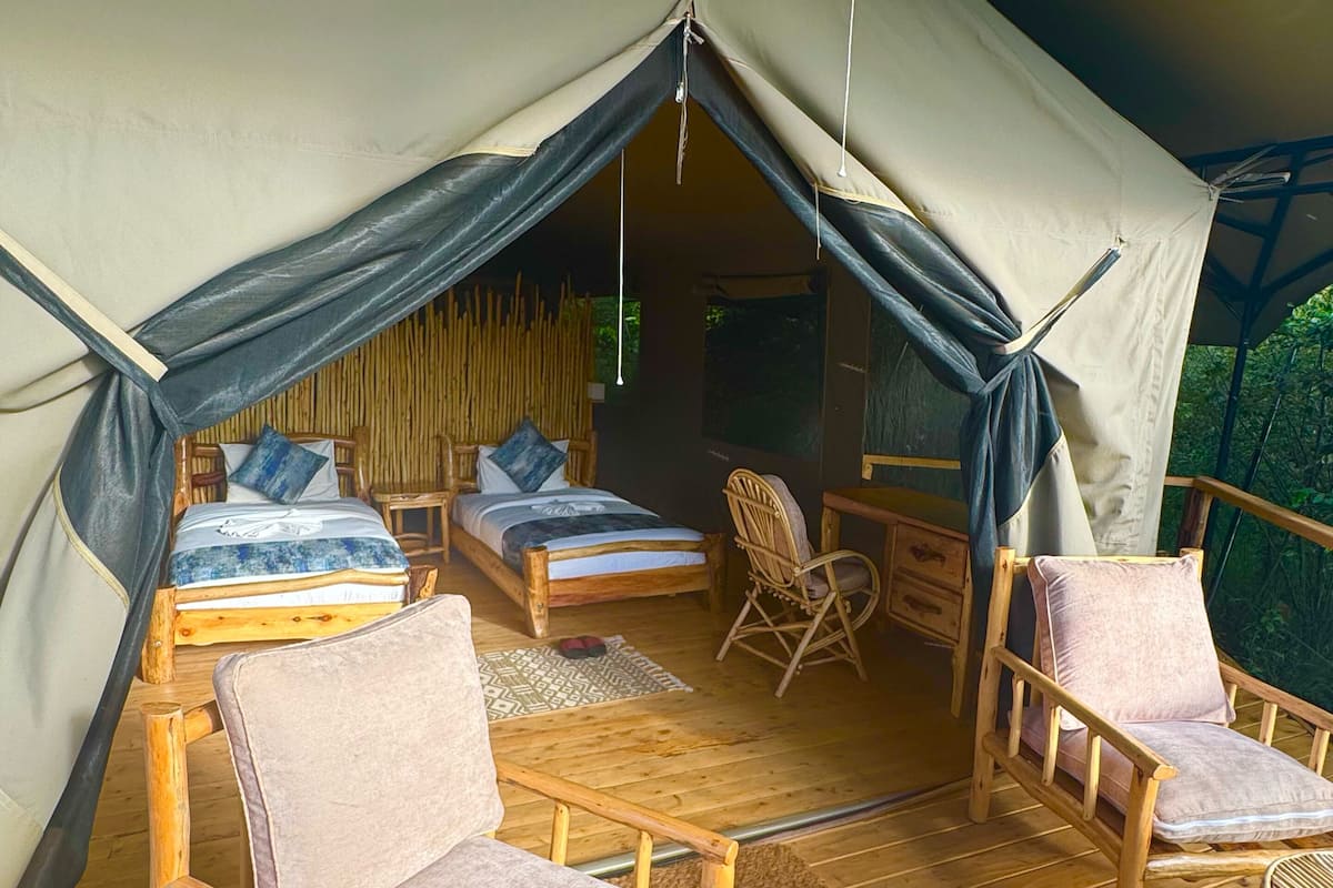 A tent with two beds, wooden furniture, and a view of the outdoors.
