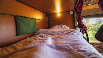 Una cama con cabecera verde, una ventana que da a zonas verdes y una cortina de cuadros rojos.