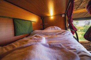 Una cama con cabecera verde, una ventana que da a zonas verdes y una cortina de cuadros rojos.