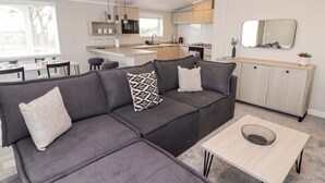 Un soggiorno moderno con un divano modulare grigio, un tavolino e una zona cucina sullo sfondo.