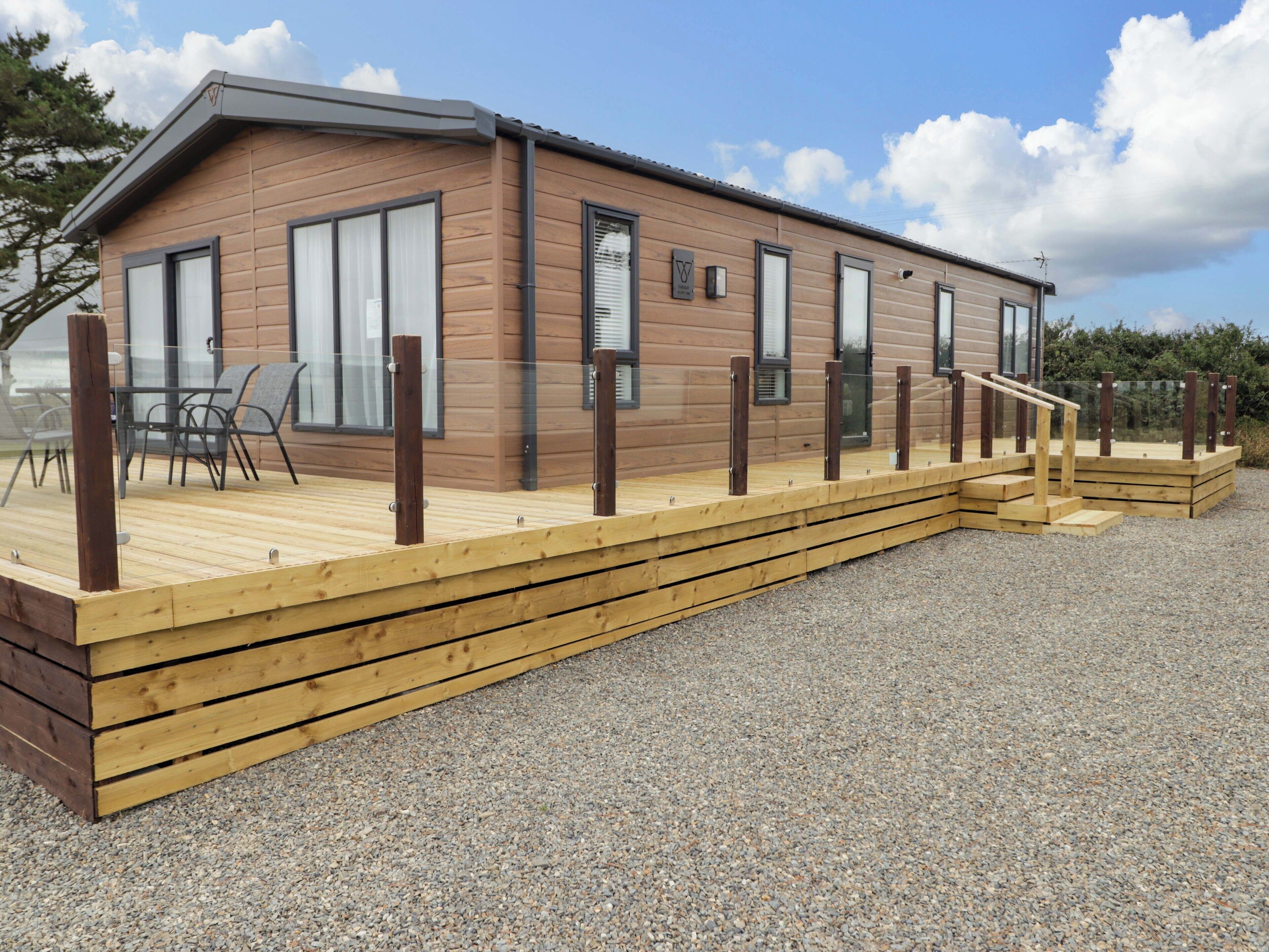 A modern wooden cabin with a deck, large windows, and a gravel ground.