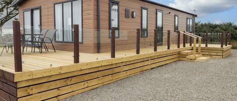 A modern wooden cabin with a deck, large windows, and a gravel ground.
