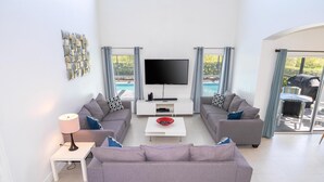 Ein modernes Wohnzimmer mit Flachbildfernseher, grauen Sofas, einem Couchtisch und Blick auf einen Pool.