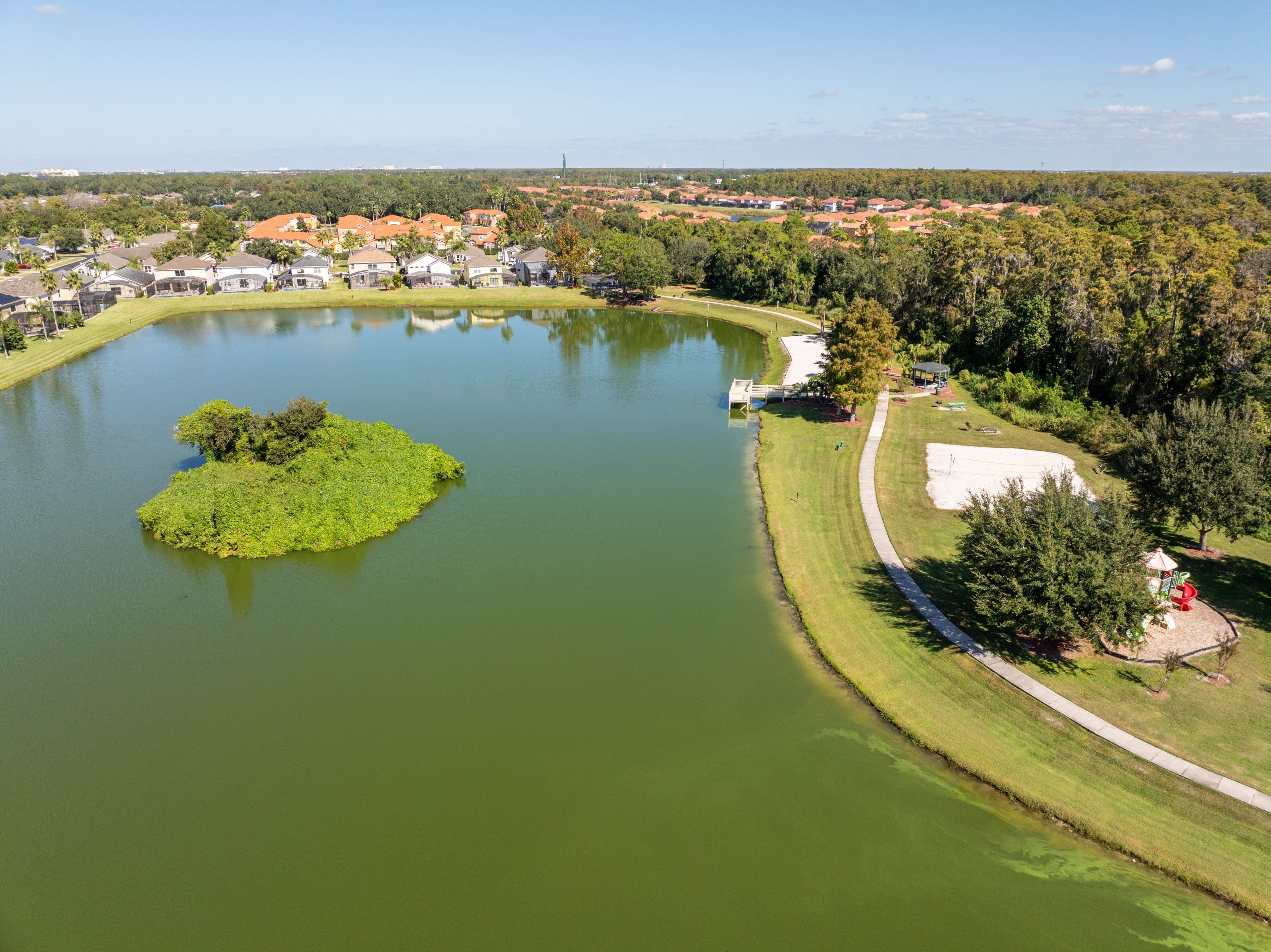 Luchtbeeld van een meer met een klein eiland, omringd door woonhuizen en begroeiing.