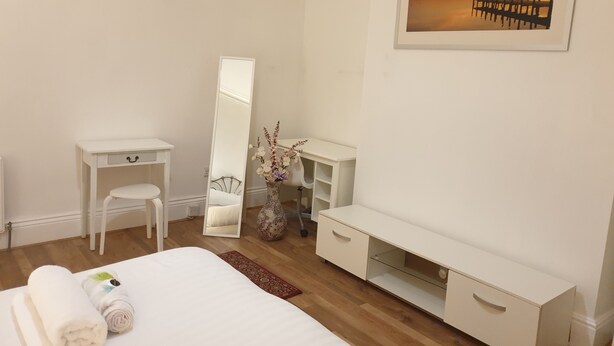 Una camera da letto con un letto, una scrivania, una sedia, un comò, uno specchio e un quadro appeso al muro.