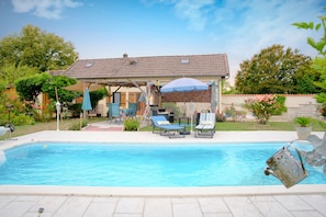 Une piscine avec des chaises longues, un patio couvert et une maison en arrière-plan.