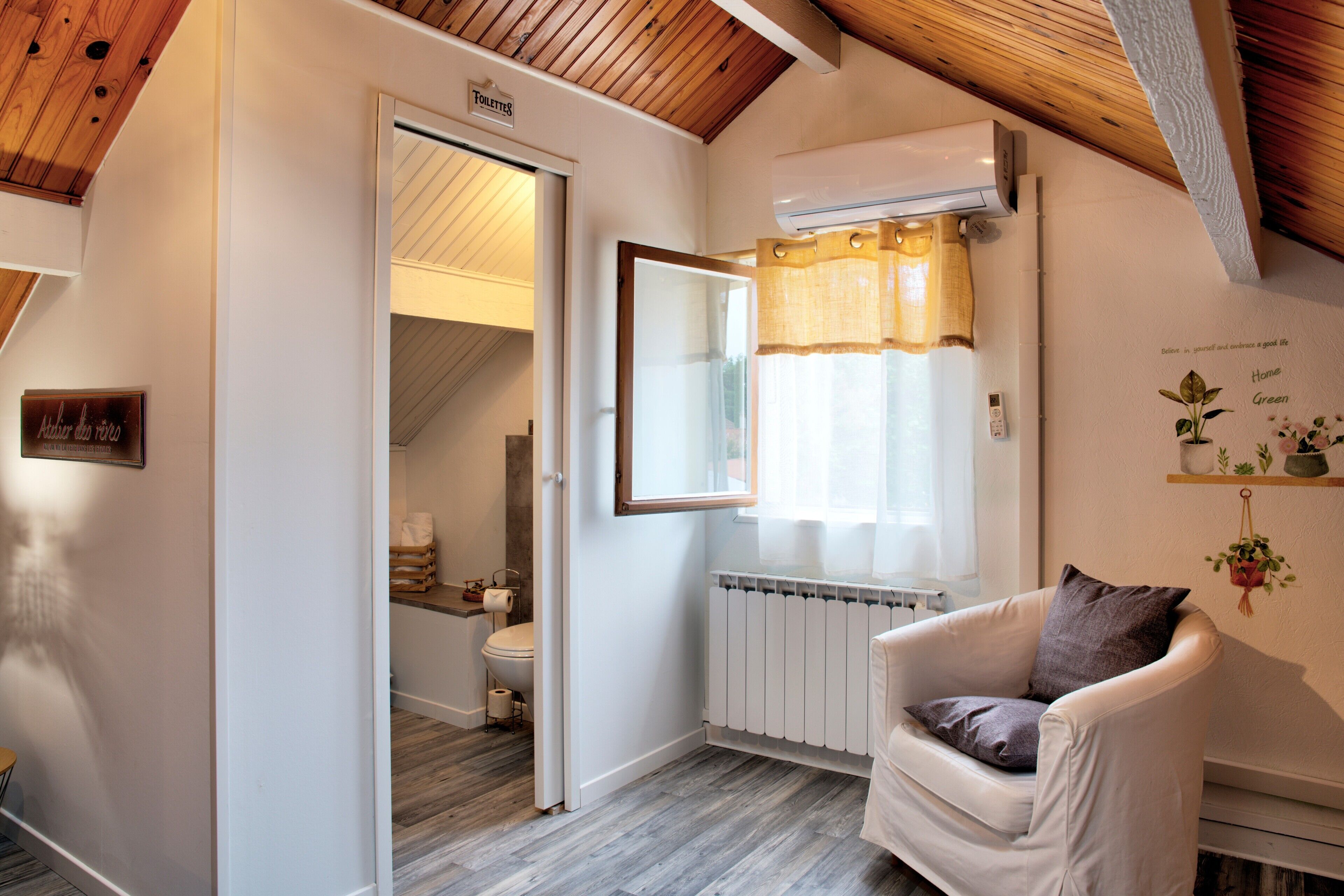 A room with a white chair, a radiator, a window with curtains, a door leading to a bathroom, and a sign above the door.