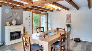 Un espace repas comprenant une table en bois, des chaises, une cheminée et une vue sur la verdure environnante.