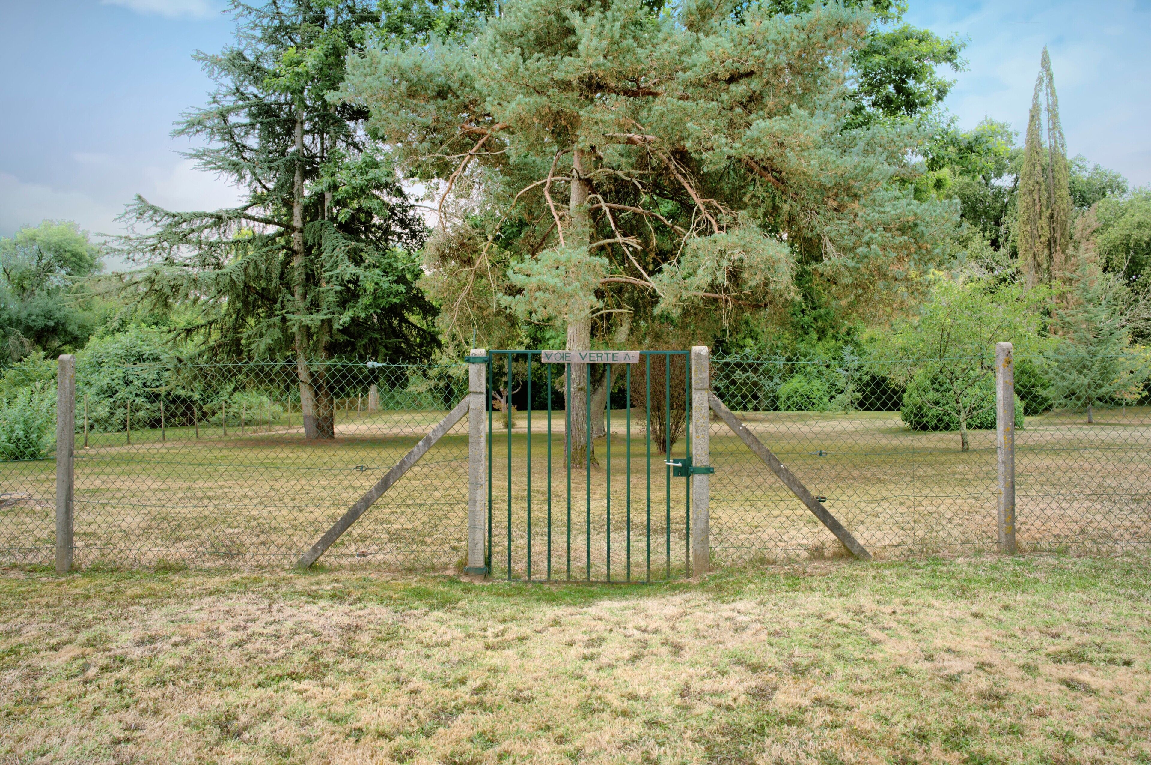 Un área cercada con una puerta, árboles y un campo cubierto de césped.