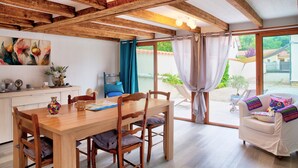 Une table à manger en bois avec des chaises, un canapé blanc et une grande fenêtre avec des rideaux.