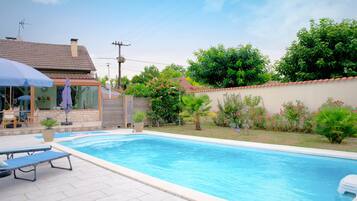 Una piscina con sillones de descanso, una zona de estar techada y un jardín con diversas plantas y flores.