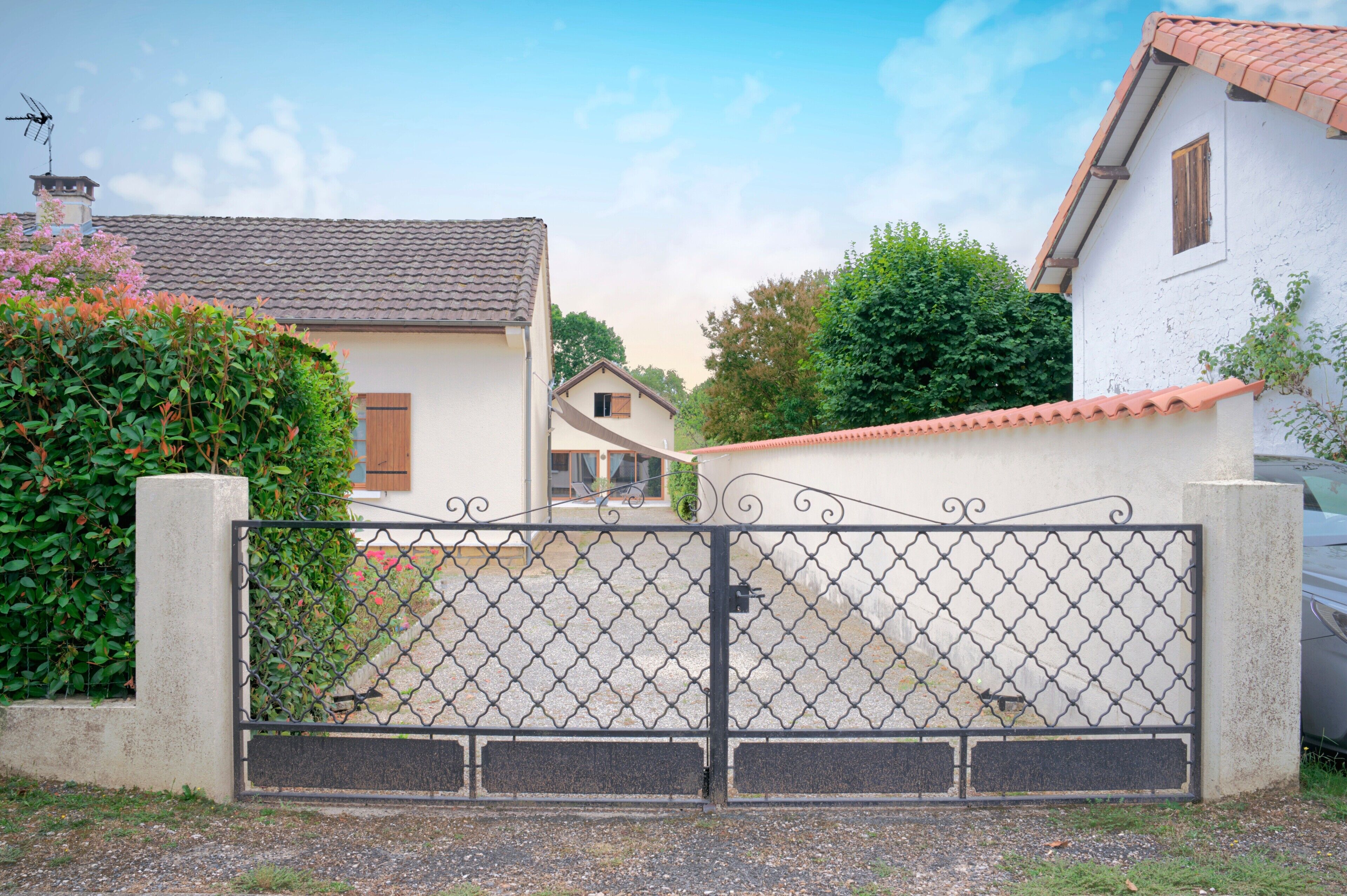 Een omheind woongebied met een huis, voorzien van een pannendak, een witte gevel en een klein raam.