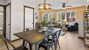 Une cuisine moderne avec une table et des chaises en bois, un ventilateur de plafond et de grandes fenêtres donnant sur la forêt.